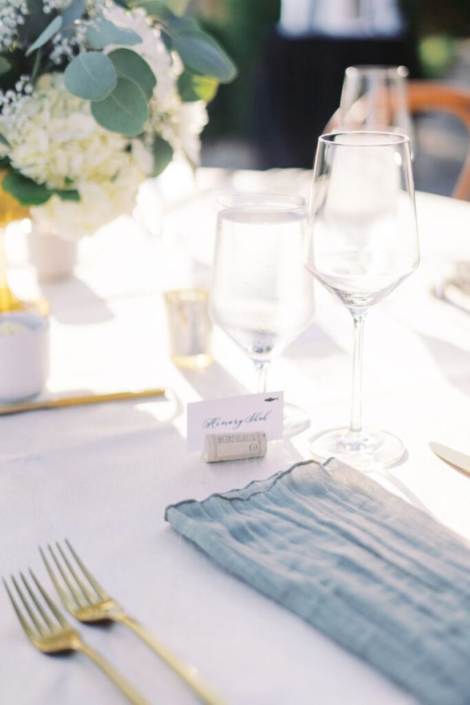 Elegant outdoor reception table featuring neutral florals, a wine glass, and soft summer light—detail captured during golden hour wedding photography