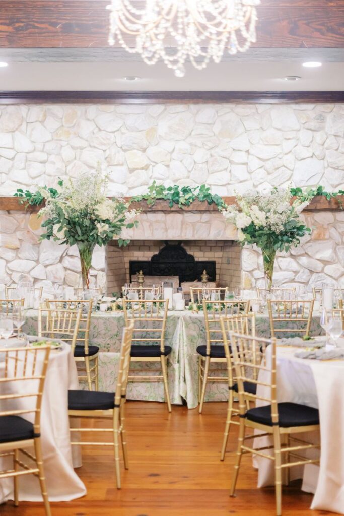 Wide photo of reception tablescape with tall florals mixed pattern table cloths and gold with black chairs, highlighting details captured during wedding day coverage